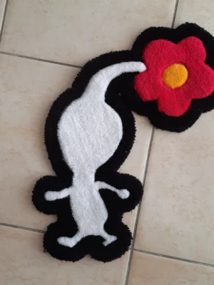 Le tapis a la forme d'un pikmin blanc avec une fleur rose éclos sur la tête. Il est moelleux et fait en laine. Il est de couleur blanche avec un contour noir. La fleur est rose fuschia avec un coeur jaune. Le Pikmin est représenté de coté en train de marcher.